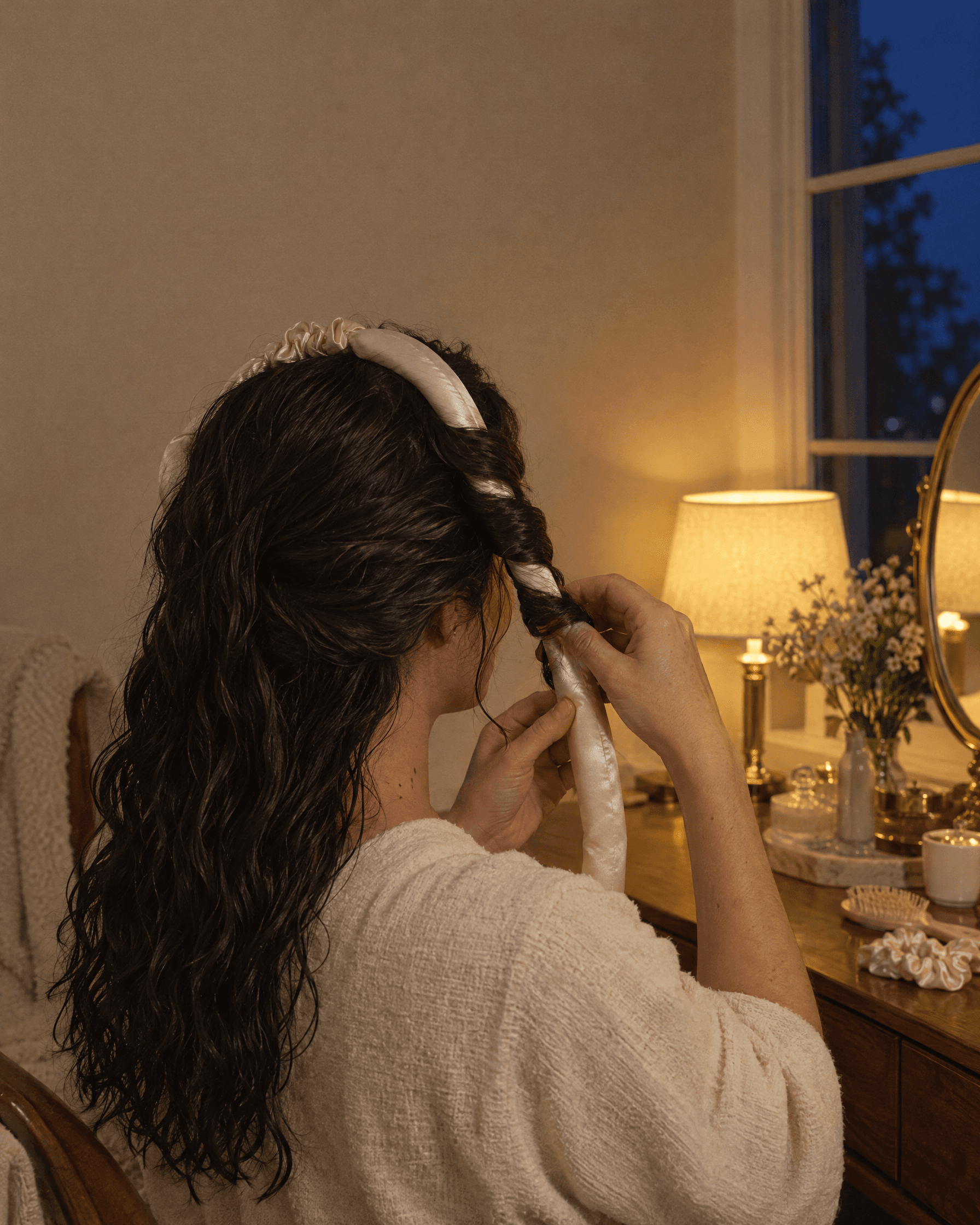 A woman seen from behind wraps a section of damp hair around a soft silk-covered rod.
